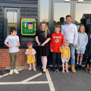 Alison Bradnick cuts the ribbon to celebrate the installation of the new defibrillator, helped by her four children Taliesin, Xander, Hermione, and Aurora and fellow residents of Walpole Meadows, Stansted