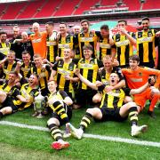 Hebburn Town players and staff celebrate with the FA Vase in front of a vast and empty Wembley Stadium.
